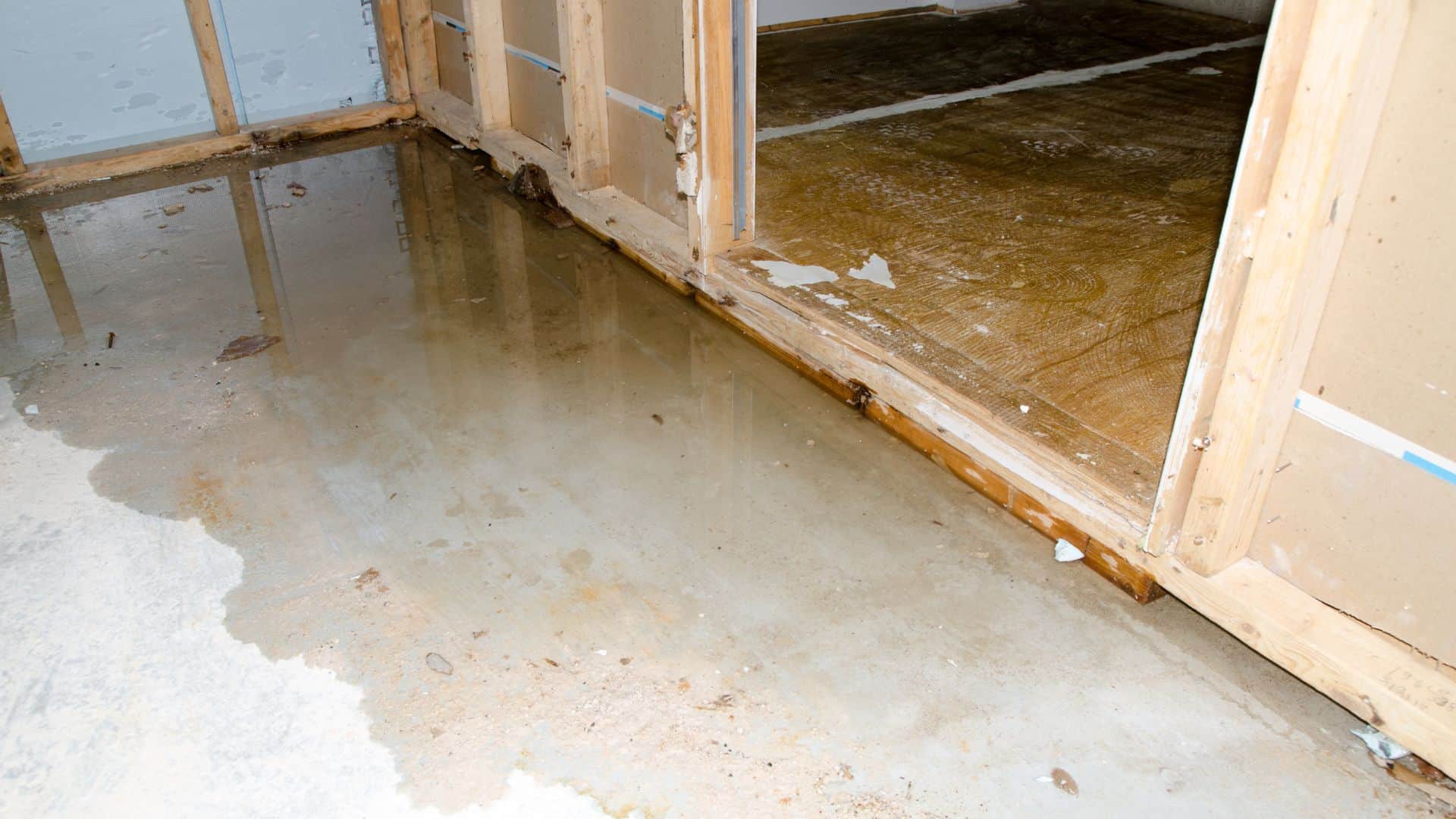 Standing water on a concrete floor near exposed wooden framing, indicating extensive water damage.